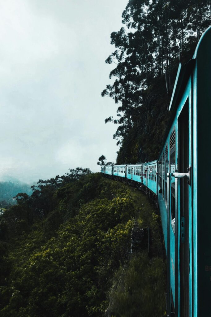 A vibrant train travels through breathtaking green hills and misty skies.